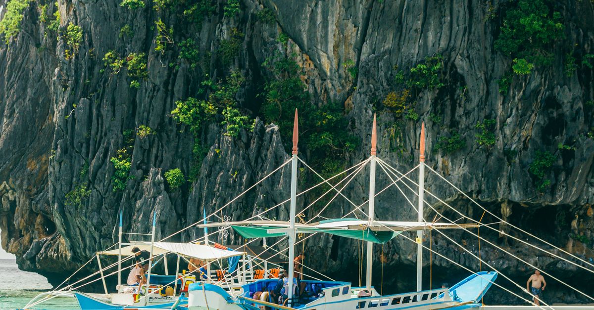 Traditional bangka boat sailing toward Big Lagoon El Nido Palawan limestone cliffs