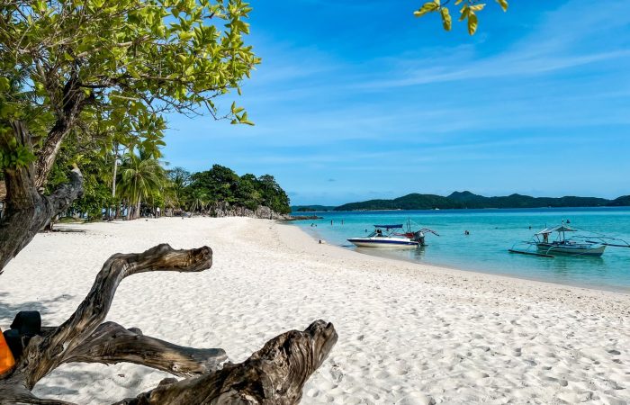 White sand beach with outrigger boats and clear blue water in Palawan, typical of Honda Bay island hopping