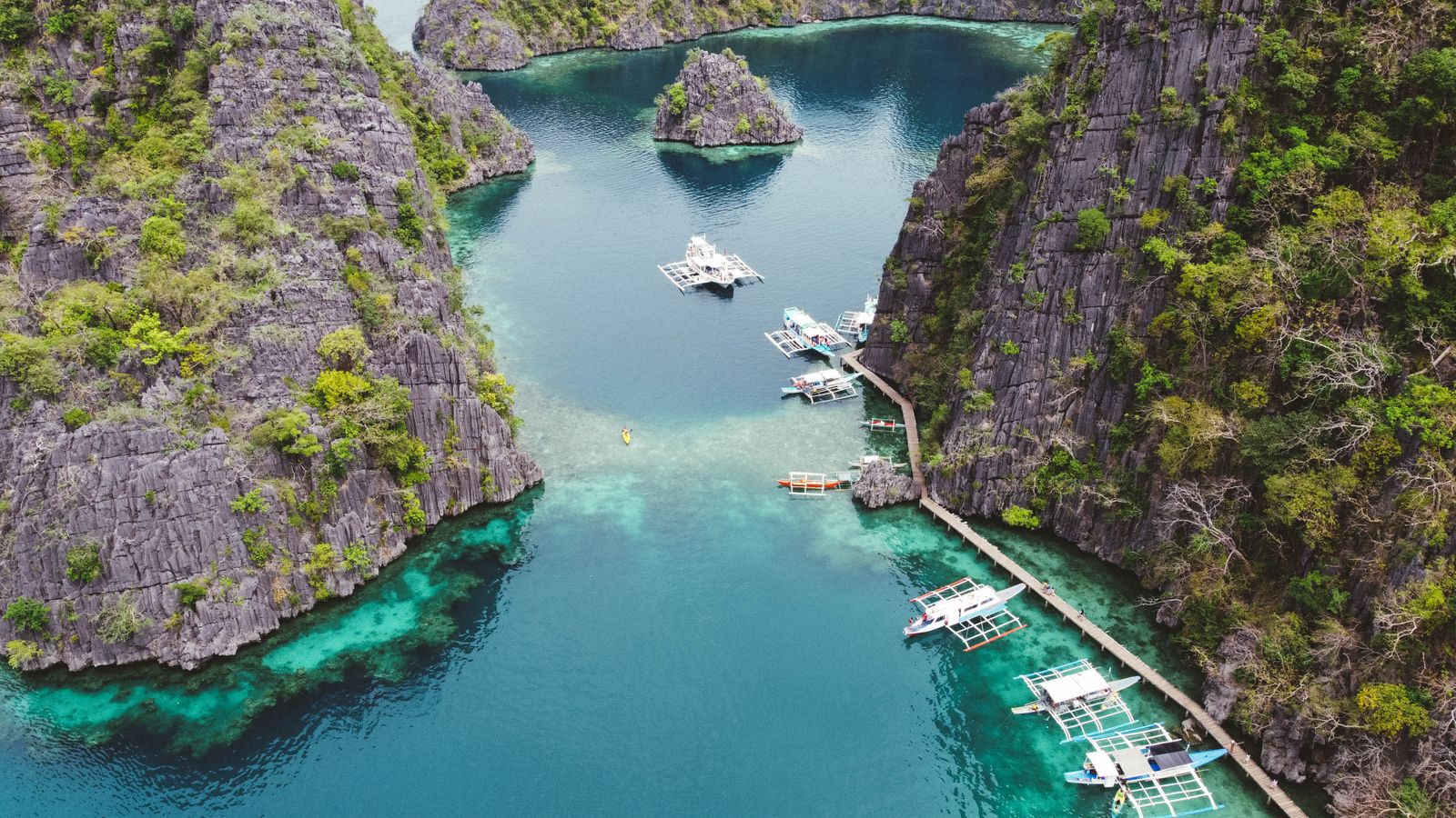 Bangka boats over clear water by limestone cliffs, Coron Palawan snorkeling stop