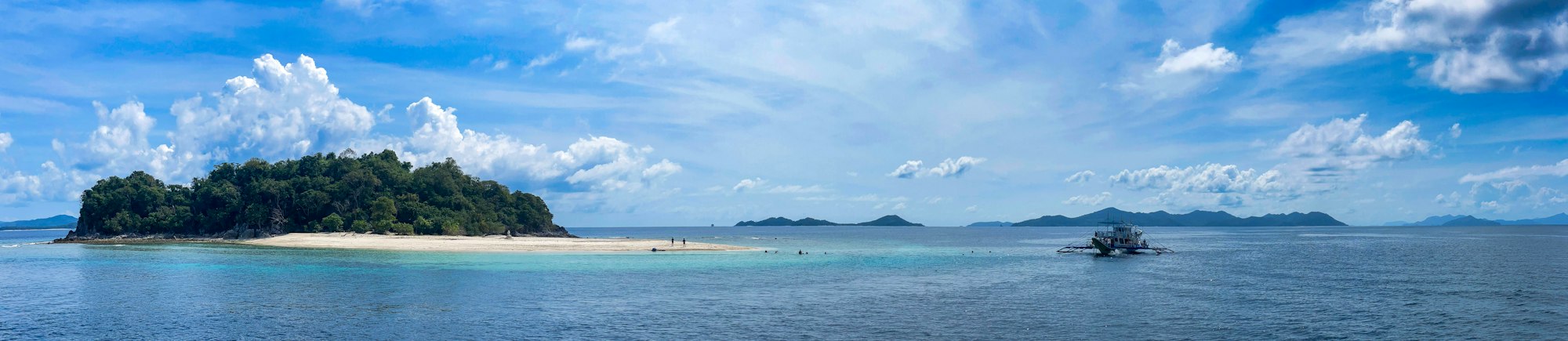 Small tropical island and shallow sandbar with swimmers in clear turquoise water, Philippines